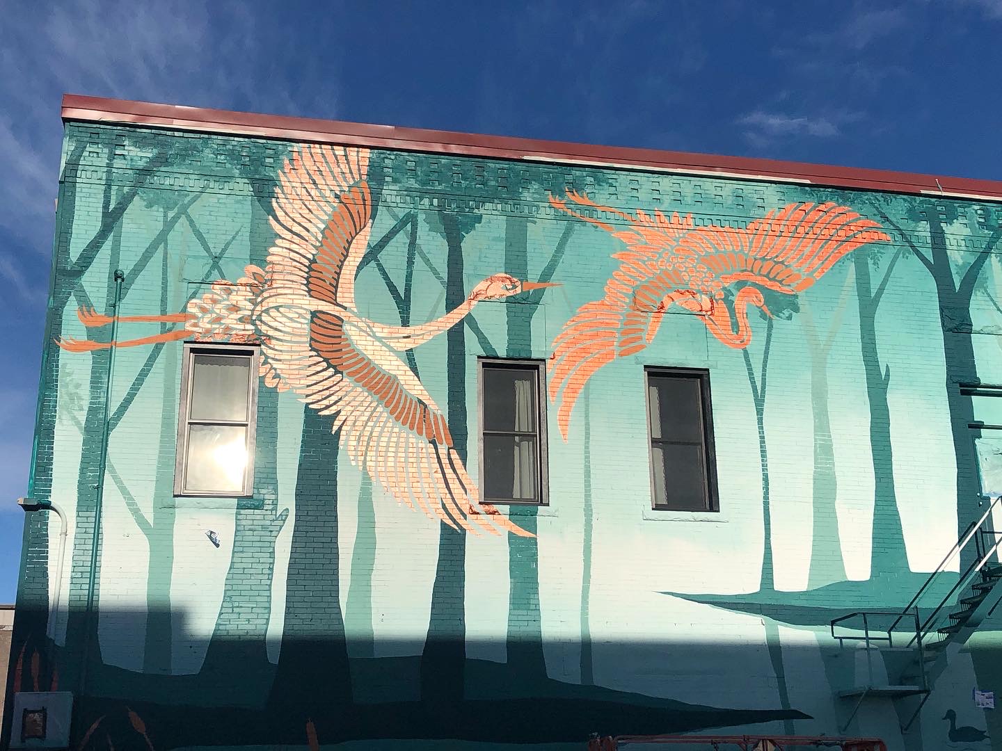 Sanctuary mural from the street: two sandhill cranes in flight across a teal forest.