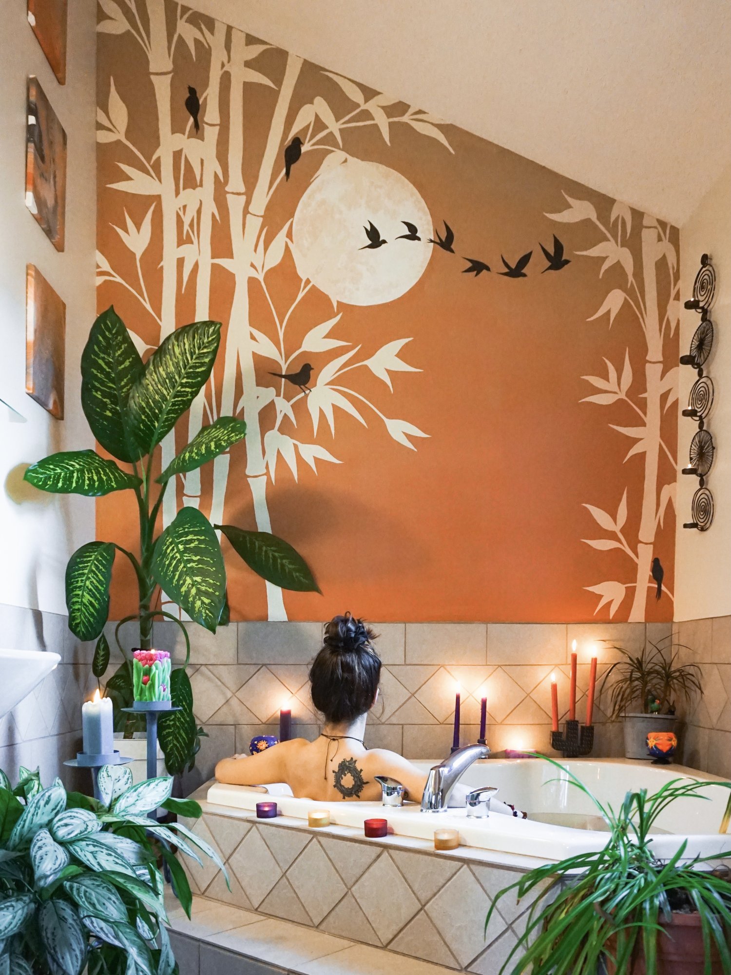 The Oasis bamboo and moon mural above a candlelit corner tub.