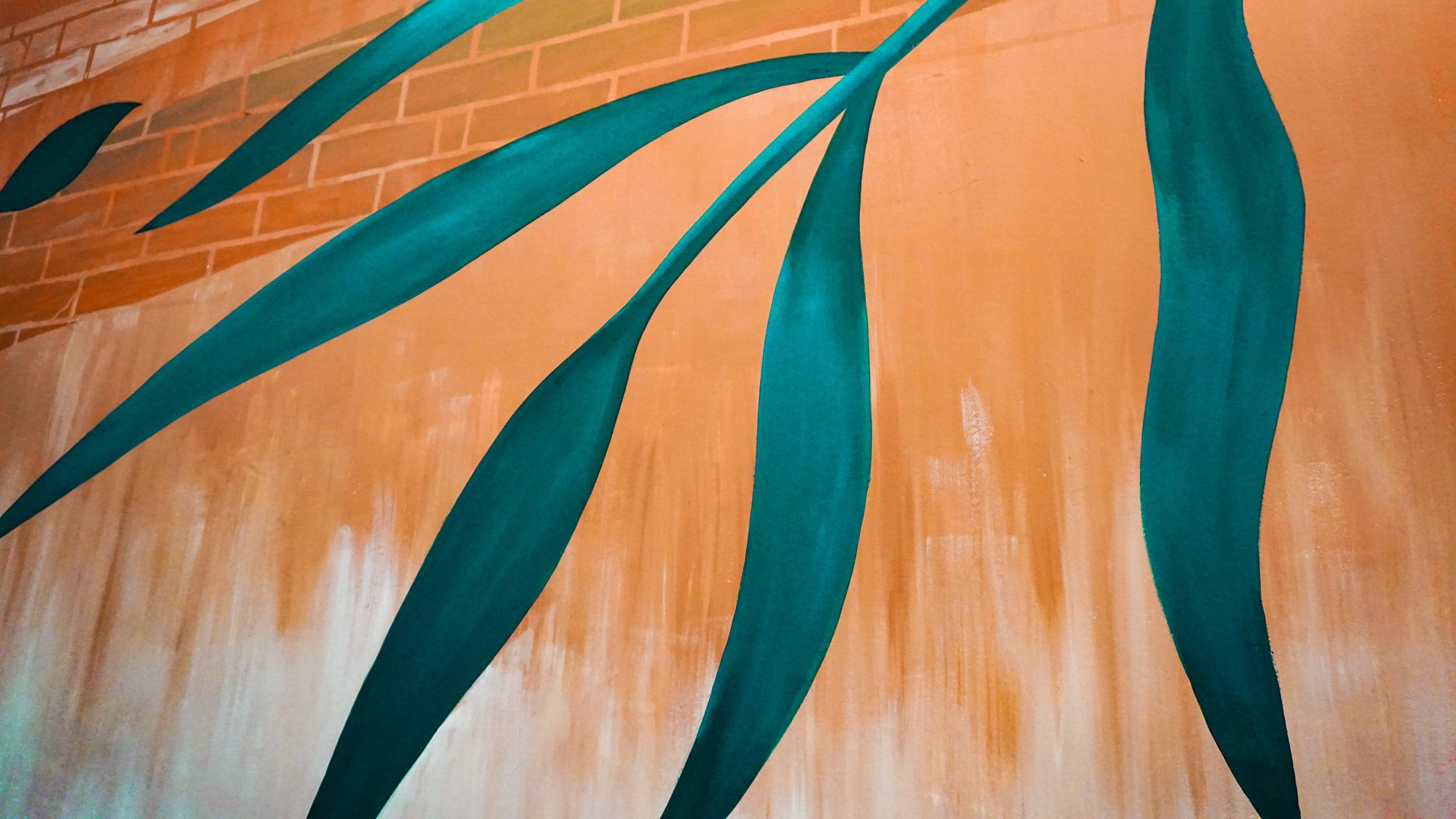 Detail of the teal botanical mural leaves against the warm ochre cafe wall.