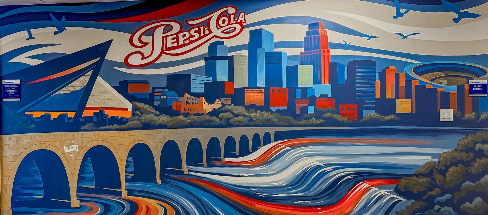PepsiCo mural of the Minneapolis skyline and Stone Arch Bridge over the river, with retro Pepsi-Cola lettering.
